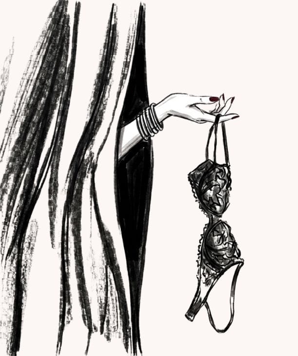 hand holding out a lace bra from behind a luxurious fitting room curtain